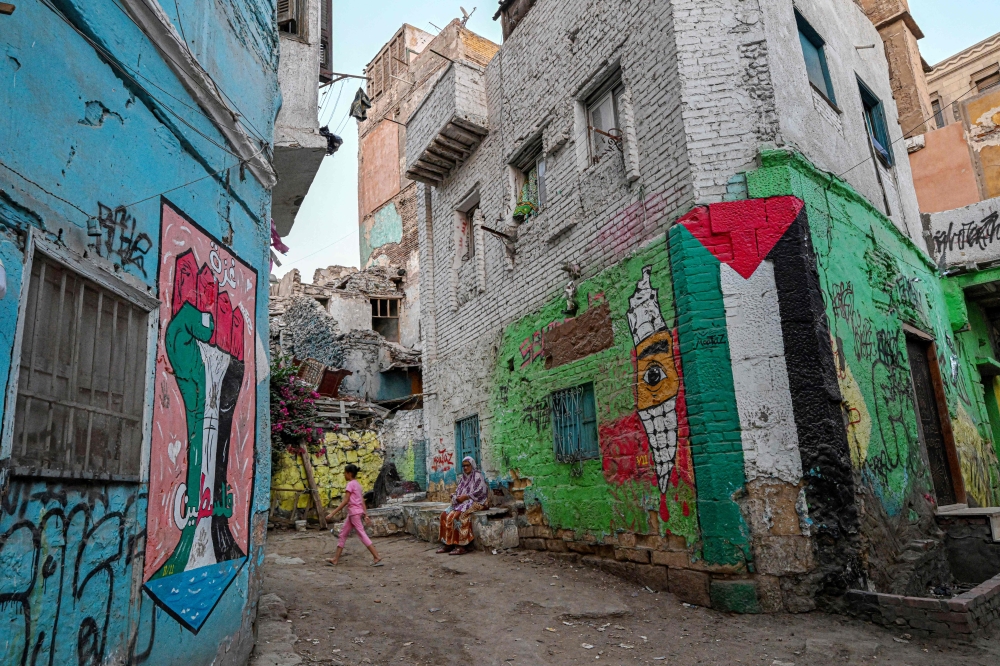 A woman sits as a girl walks past graffiti depicting the Palestinian flag in solidarity with the people of Gaza in the Darb al-Ahmar district in Cairo on May 28, 2024. — AFP pic
