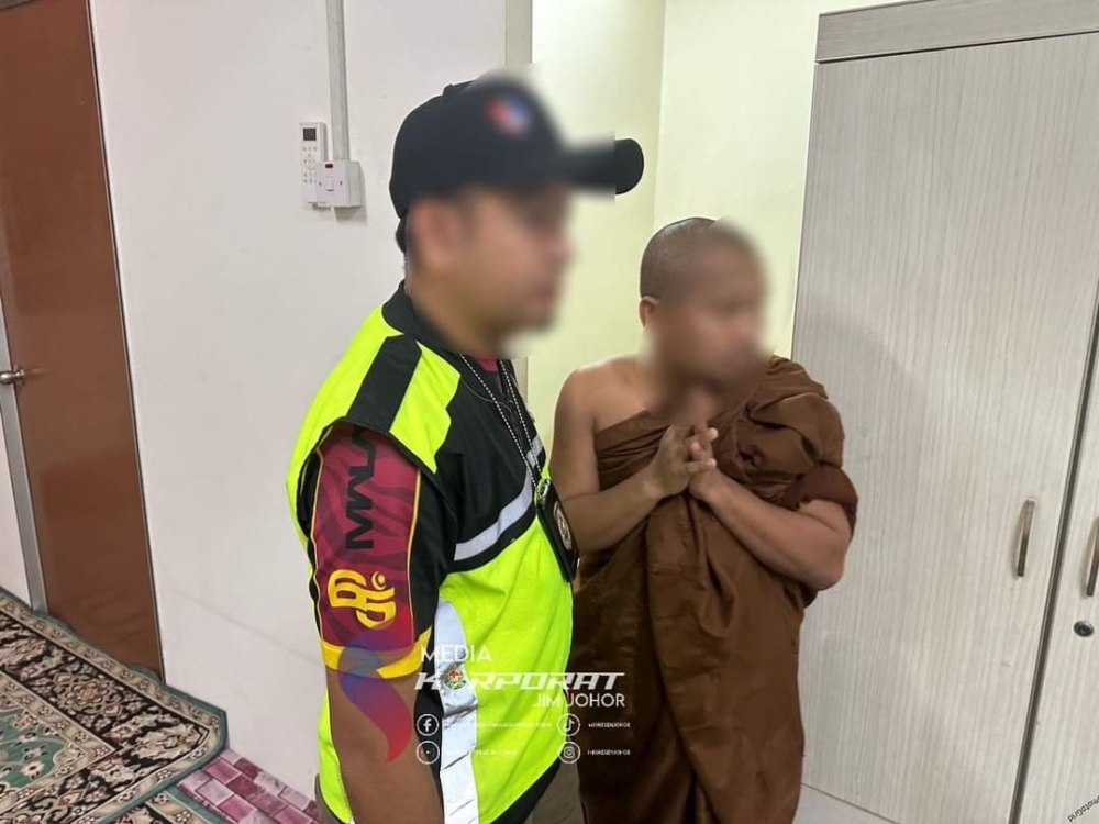 A Johor Immigration Department enforcement officer with a caretaker of a worship centre who was arrested this morning for working illegally in Taman Setia Indah, Johor Baru. — Picture by the Johor Immigration Department