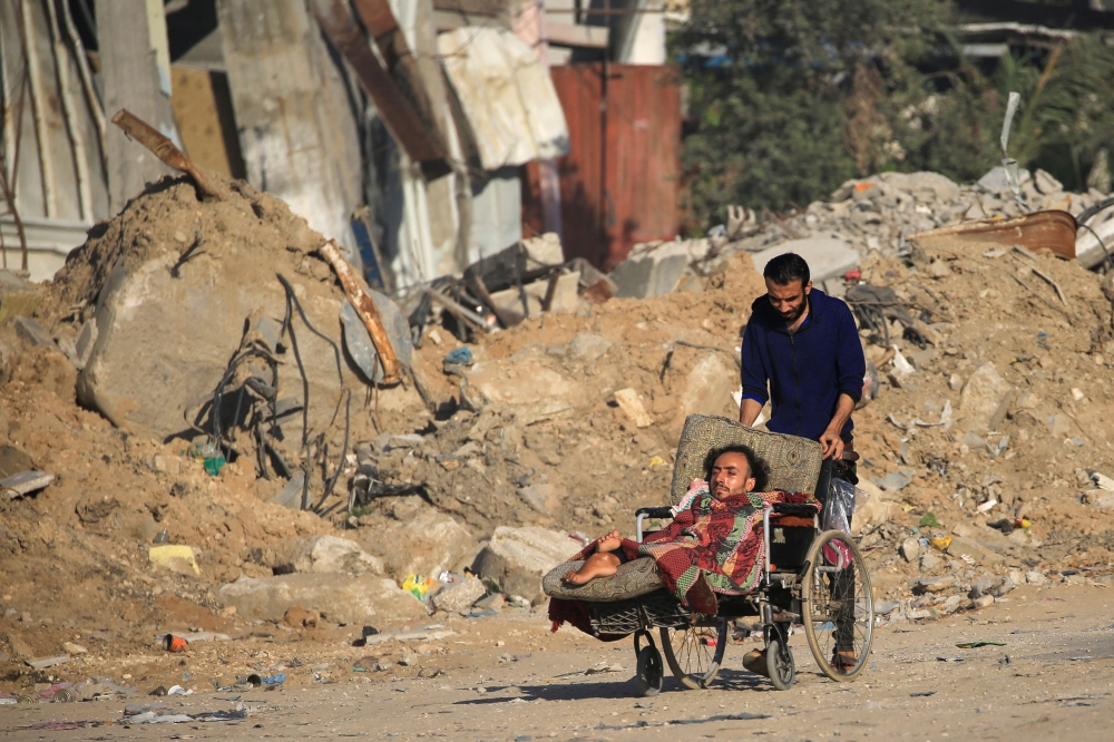 A Palestinian man pushes another on a wheelchair past building rubble at al-Maghazi refugee camp in the central Gaza Strip on June 5, 2024, amid the ongoing conflict between Israel and the Palestinian militant group Hamas. — AFP pic