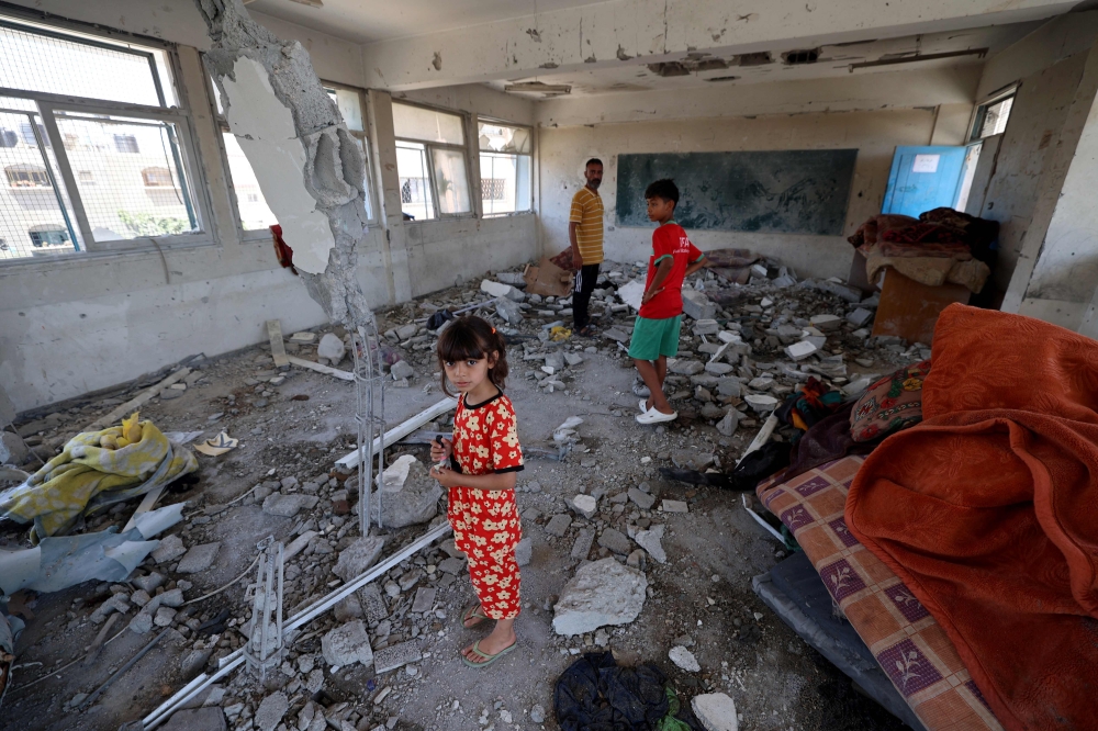 A Palestinian girl stands with her brother in the destroyed classroom at a school run by the UN Relief and Works Agency for Palestine Refugees (UNRWA) which was hit during an Israeli army strike the day before, in the Nuseirat camp in the central Gaza Strip on June 7, 2024, amid the ongoing conflict in the Palestinian territory between Israel and Hamas. ― AFP pic