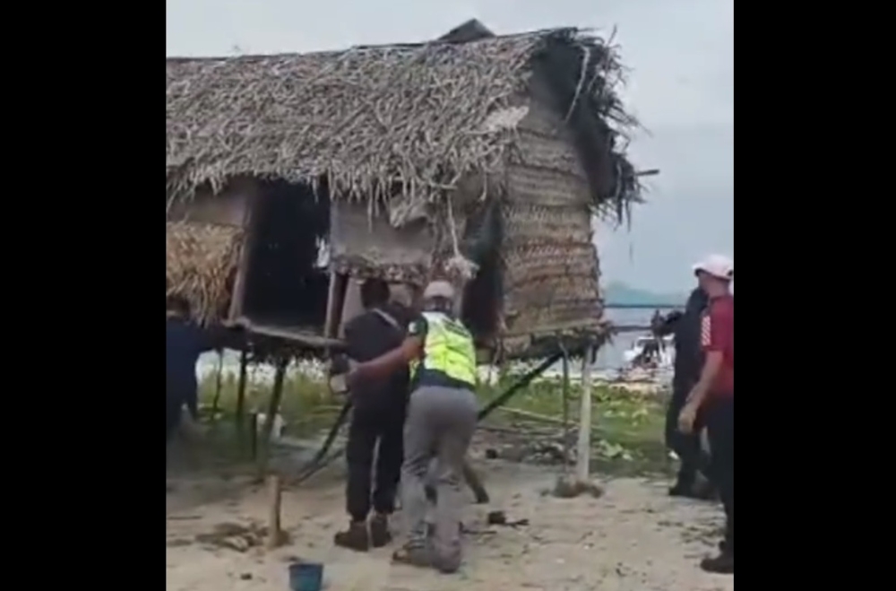 File picture of a video posted by Borneo Komrad on social media showing several men, some in uniform, smashing a wooden hut on a beach with large sticks before burning it down. — Screengrab from Facebook/Borneo Komrad