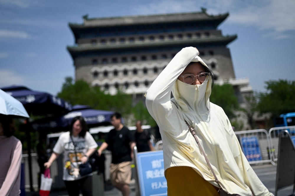 A woman shelters under her cloth as she visits a business street on a hot day in Beijing on June 11, 2024. — AFP pic