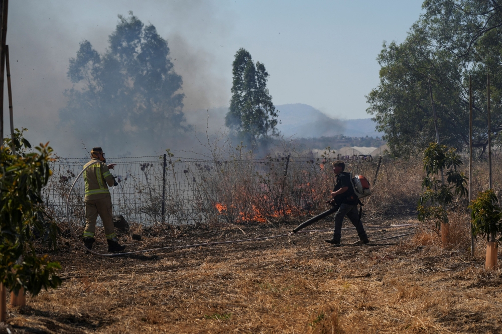 Israeli fire-fighter and another man work to take control over fire following rocket attacks from Lebanon, amid ongoing cross-border hostilities between Hezbollah and Israeli forces, in the Israeli-occupied Golan Heights, June 11, 2024. — Reuters pic