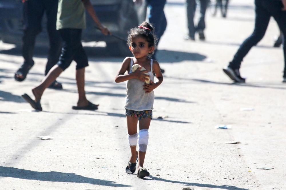 A Palestine child holding a loaf of dough as she walks down a street in Deir al-Balah in central Gaza. — AFP pic