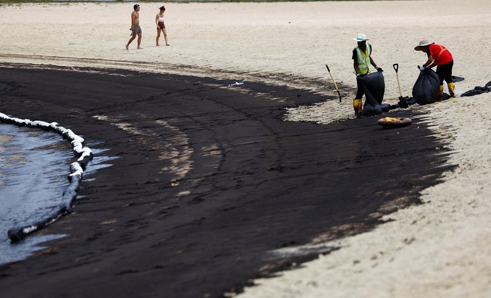 Workers clean up the beach following an oil slick, at Tanjong Beach in Sentosa, Singapore June 15, 2024. — Reuters pic