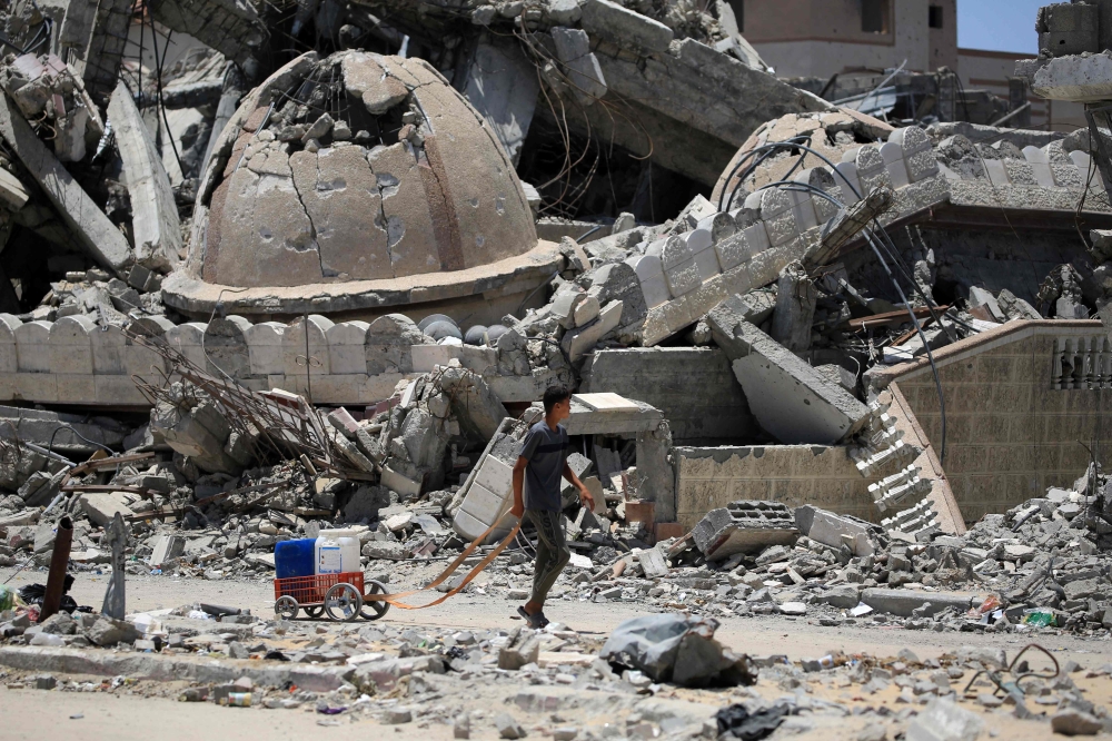 File photo of a young Palestinian transporting water walking past a destroyed mosque in Khan Younis in the southern Gaza Strip on June 14, 2024, amid the ongoing conflict between Israel and the Palestinian Hamas militant group. — AFP pic