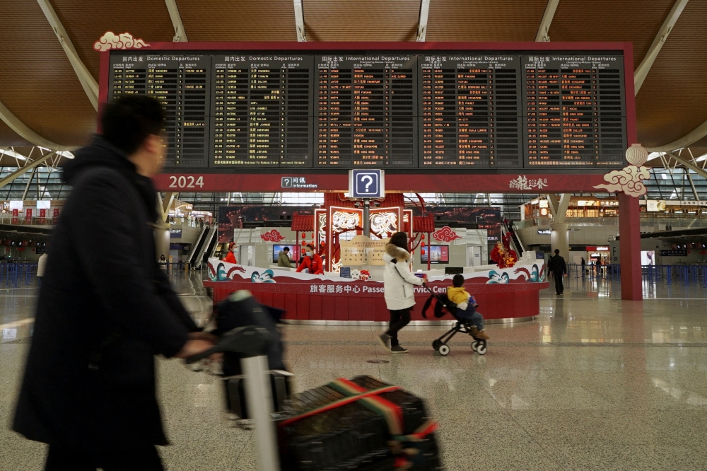 Travellers walk past a display showing departure flights information at Shanghai Pudong International Airport during the Spring Festival travel rush on Lunar New Year's Eve, in Shanghai, China February 9, 2024. — Reuters file pic