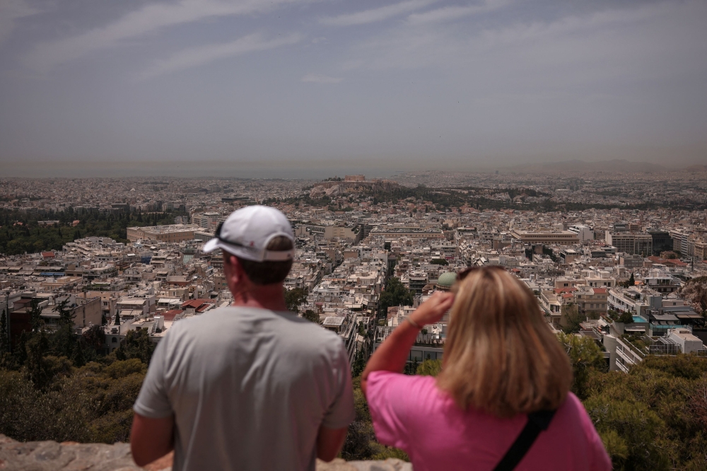 Tourists look at Athens from atop Lycabettus hill, as Saharan dust blankets the city in the background during a heatwave in Athens, Greece, June 13, 2024. — Reuters pic