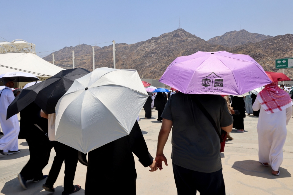 Muslim pilgrims hold hands as they walk with umbrellas to the site where people take part in the Satan stoning ritual, during the annual haj pilgrimage in Mina, Saudi Arabia June 18, 2024. — Reuters pic