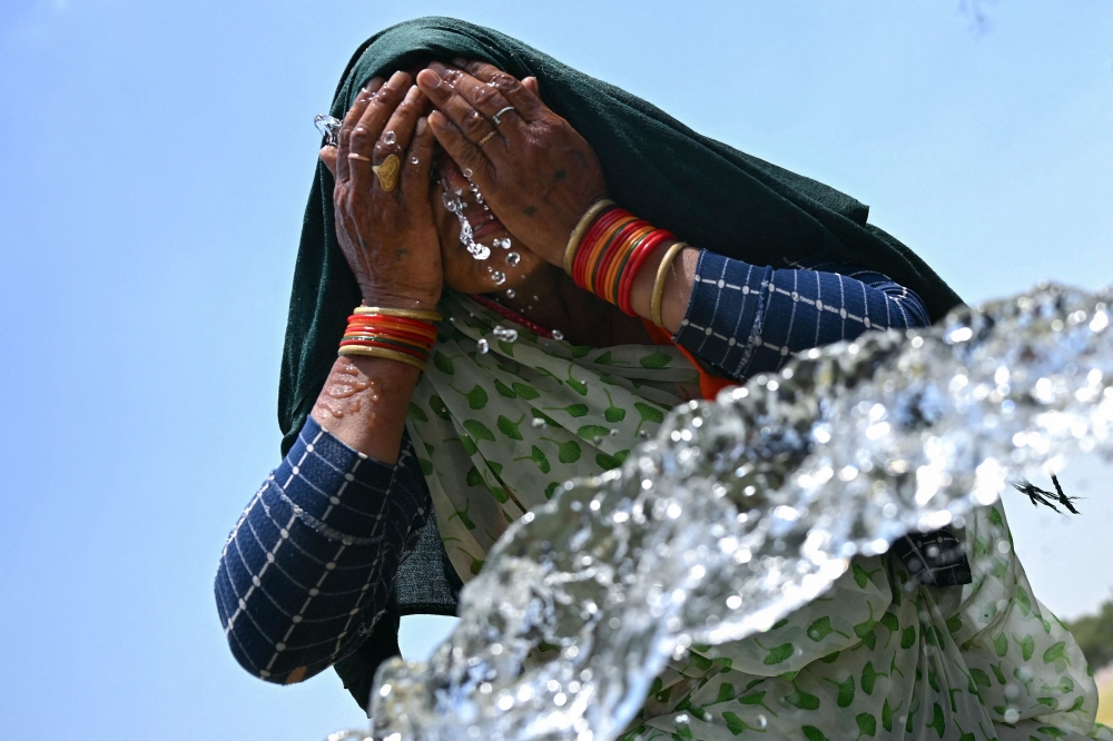 A woman washes her face with water to cool off during a hot summer day near the India Gate in New Delhi on June 17, 2024. — AFP pic