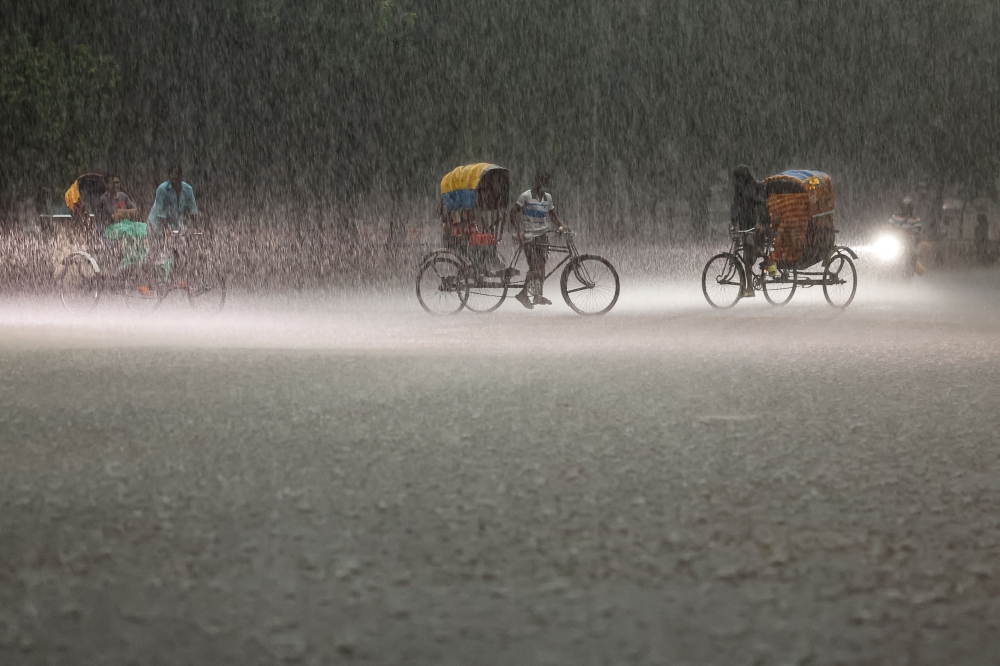 People ride on rickshaws during a downpour in Dhaka, Bangladesh, June 13, 2024. — Reuters pic