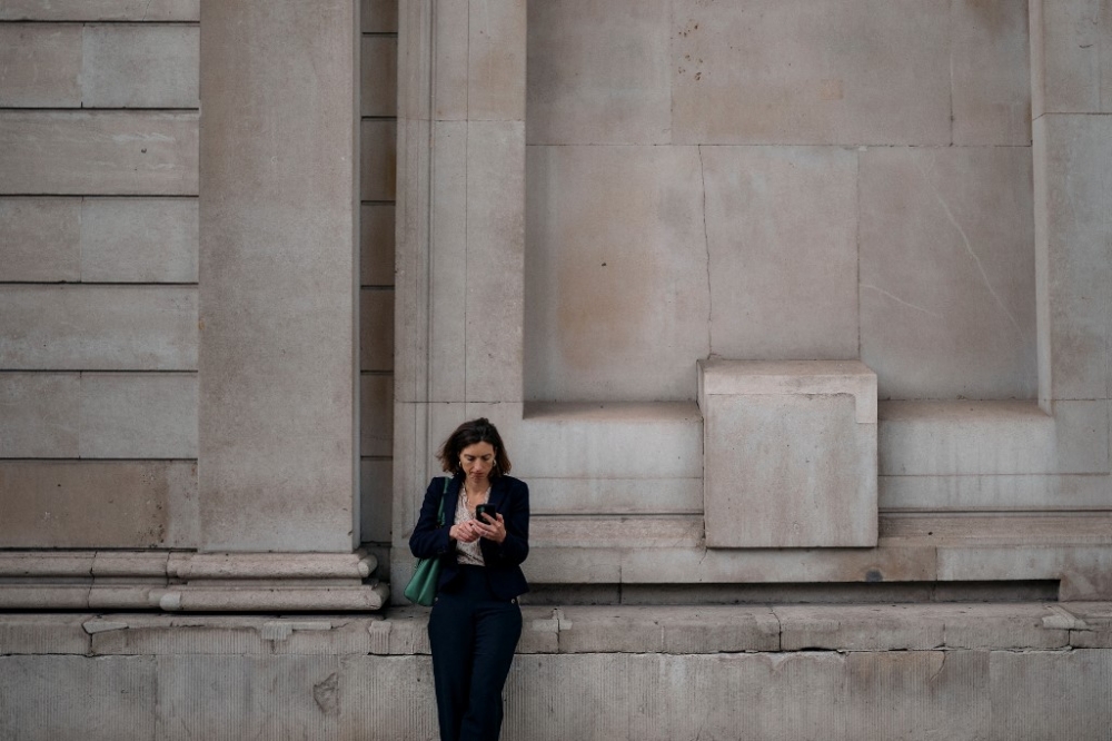 A woman looks at her phone as she stands in front of the Bank of England in The City financial district, in central London, on June 12, 2024. — AFP pic