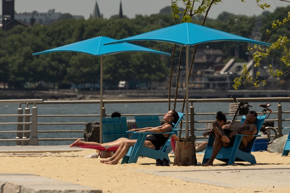 People sit along the Hudson River during a heatwave on June 20, 2024 in New York City. — AFP pic