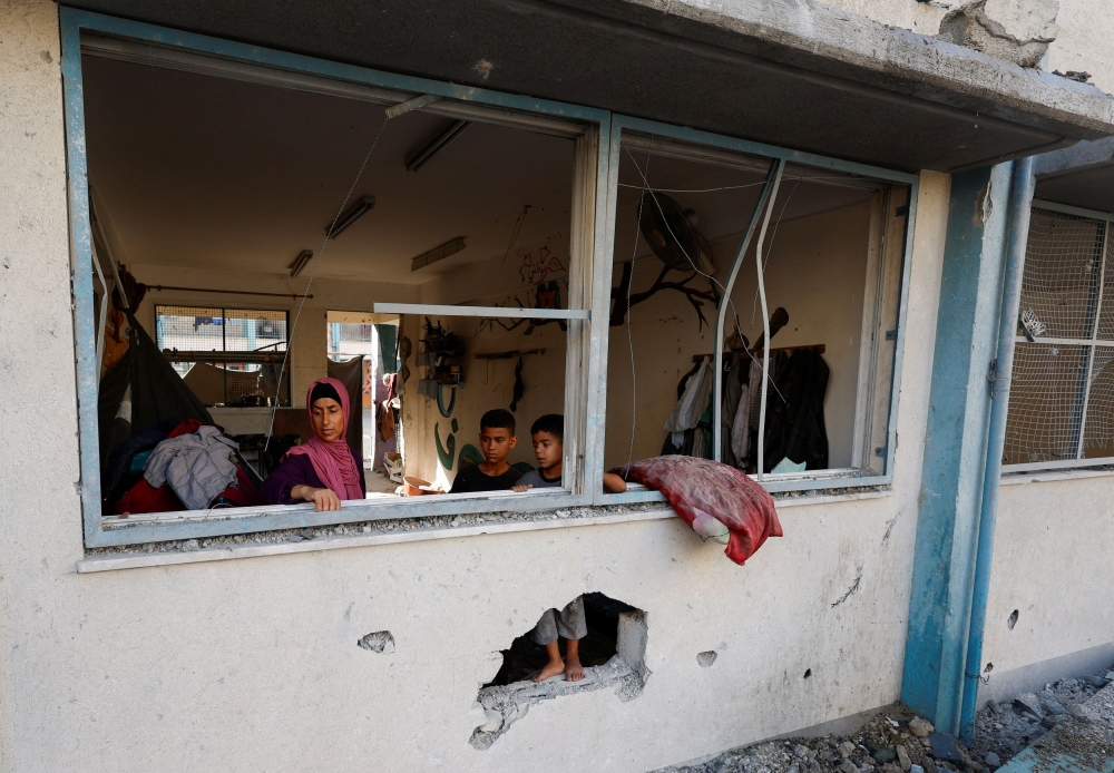 Palestinians stand near the damaged windows of a classroom in a UNRWA school, after the air strike on a neighbouring house to the school in Khan Younis, in the southern Gaza Strip, June 21, 2024. ― Reuters pic