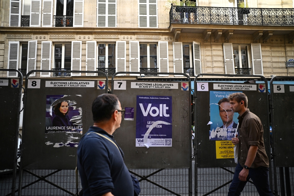 People walk past election posters outside a polling station, ahead of the French parliamentary elections, in Paris, France, June 22, 2024. — Reuters pic
