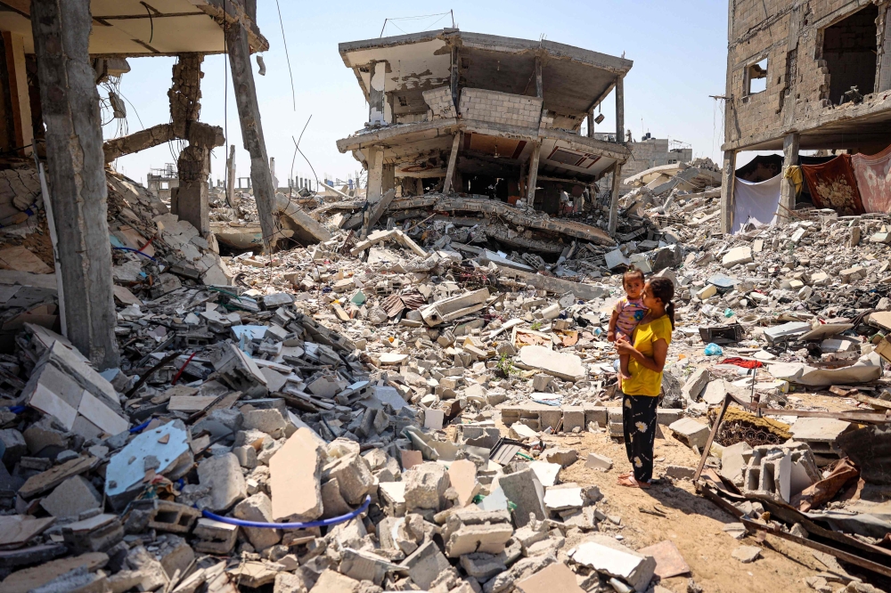 Palestinian children surrounded by the rubble of buildings destroyed during Israeli bombardment in Khan Yunis. — AFP pic
