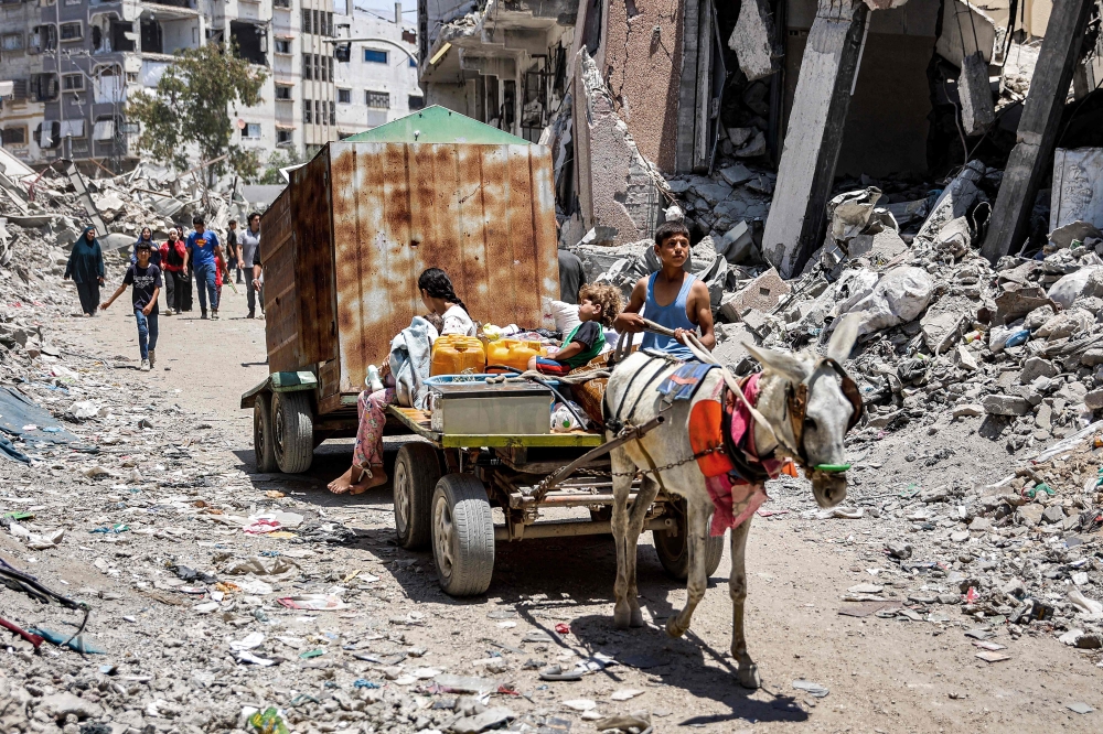 A boy drives a donkey-drawn cart carrying two children, jerrycans, sacks of flour, and other items while evacuating from the Tuffah neighbourhood in the east of Gaza City heading towards areas in the west, on June 24, 2024 amid the ongoing conflict in the Palestinian territory between Israel and Hamas. — AFP pic
