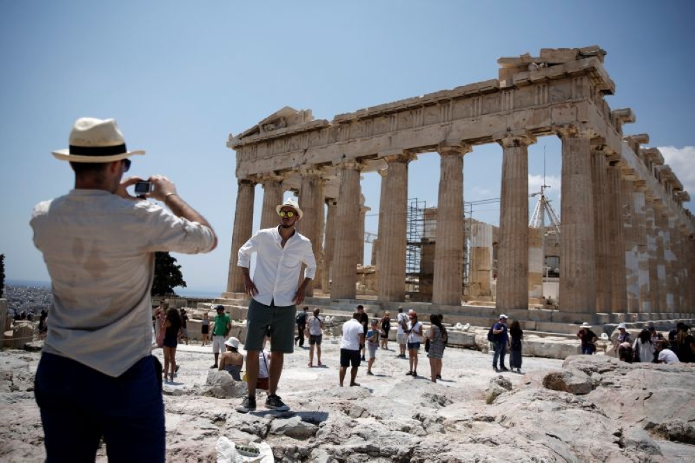 A tourist poses for a picture in front of the ancient Parthenon temple atop Acropolis hill in Athens July 19, 2017. — Reuters pic