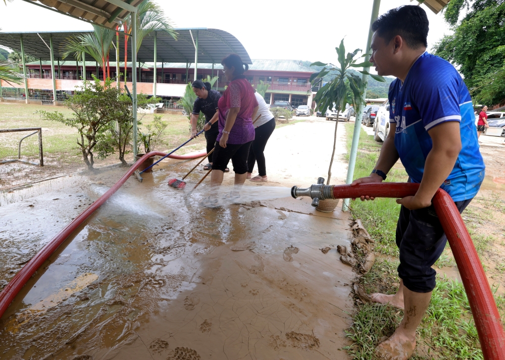 Teachers of St Michael Secondary School in Penampang participate in a collective effort to clean the school grounds on July 3, 2024, following last Sunday’s severe flooding. — Bernama pic