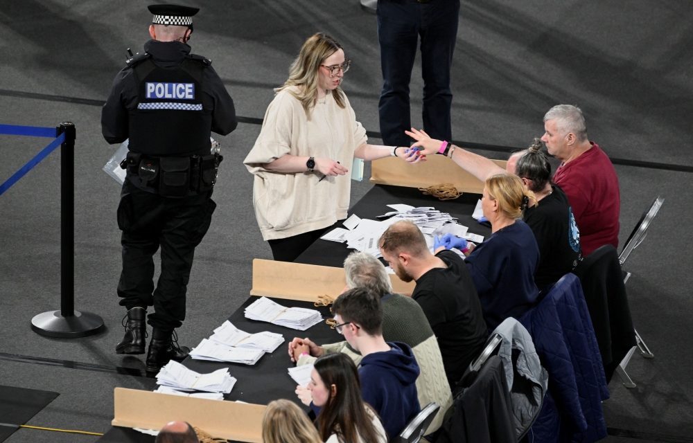 A poll staff member hands forensic gloves to another as police officers look into possible impersonation fraud during the UK election in Glasgow, Scotland, Britain, July 4, 2024. — Reuters pic