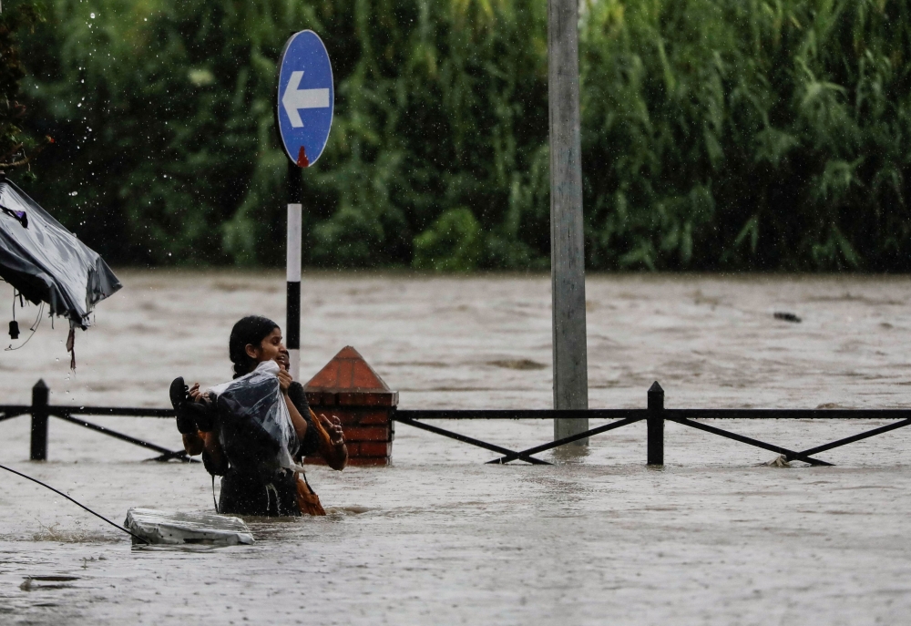 A woman carrying her belongings wades through a flooded road along the bank of the overflowing Bagmati River following heavy rains in Kathmandu. — Reuters pic