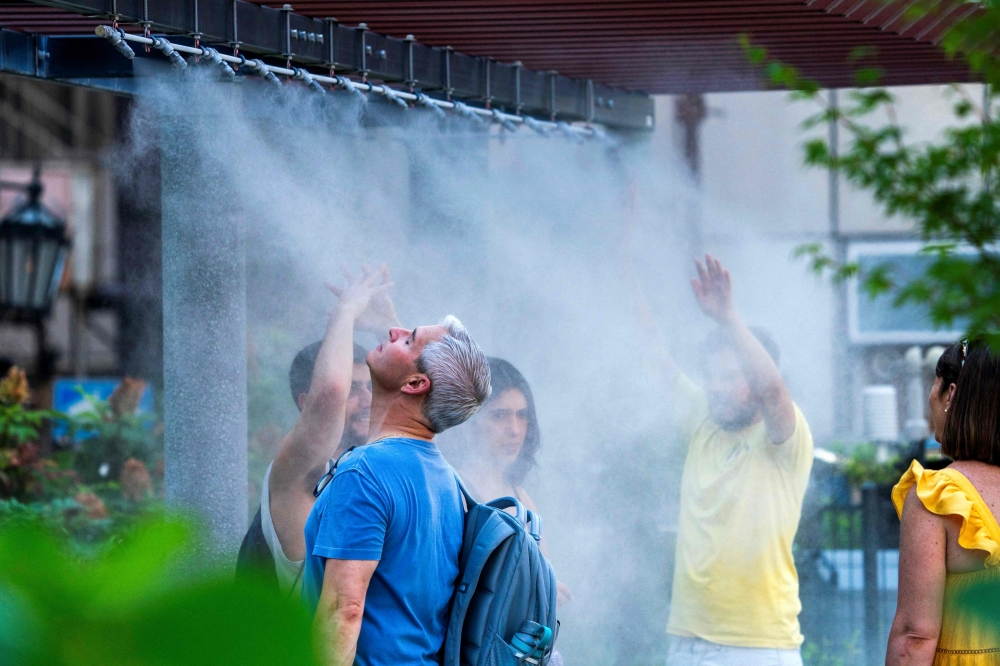 Tourists cool down under a mist shower in central Tokyo where temperatures have topped 35 degrees Celsius on July 8, 2024. — AFP pic