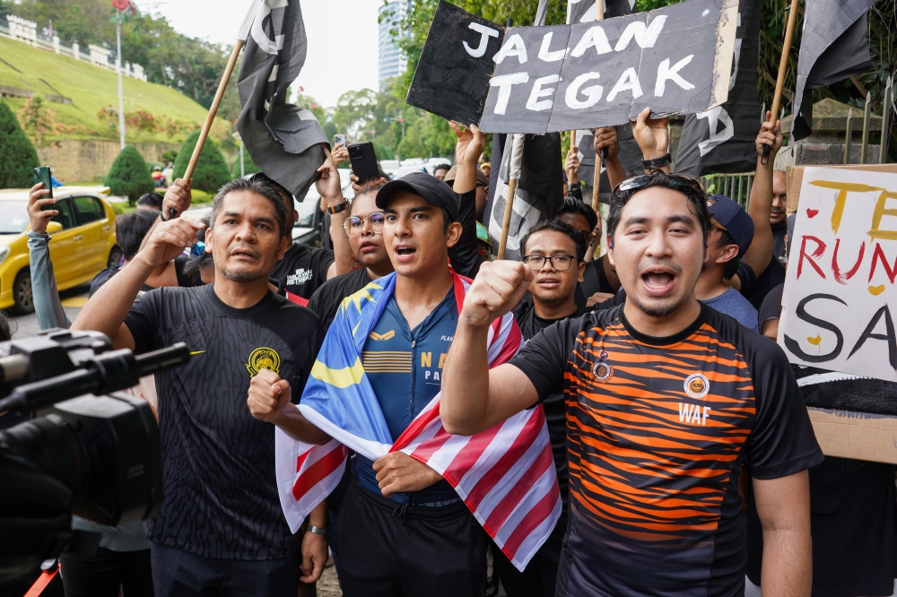 Syed Saddiq Abdul Rahman (wrapped in flag) poses outside Parliament after completing a run from his Muar constituency on July 1, 2024. — Picture by Shafwan Zaidon