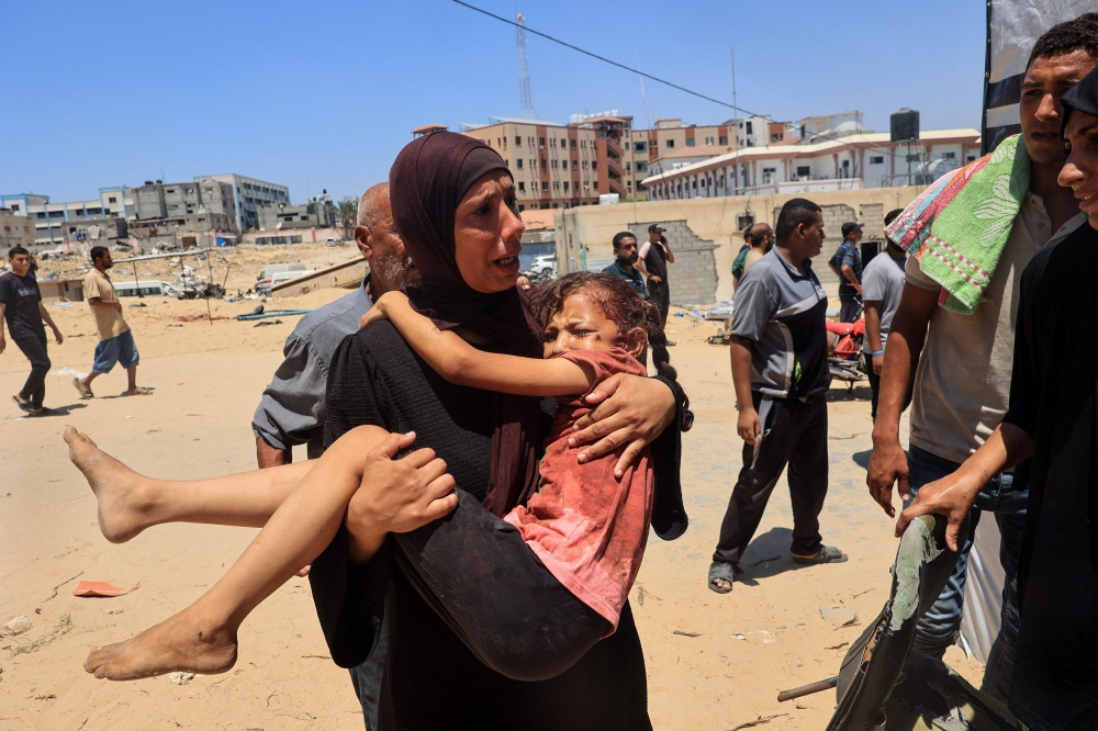 A Palestinian woman carries an injured child to the Nasser hospital in Khan Yunis on July 13, 2024, one of the health establishments to which casualties were rushed after an Israeli strike killed at least 71 people and injured many others at the al-Mawasi camp for the war displaced in the south of the Palestinian territory, according to the Hamas-run health ministry. — AFP pic