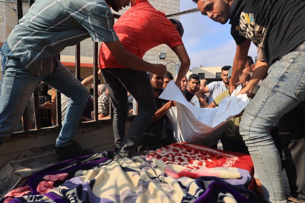 Relatives load a victim onto the back of a truck to be taken for burial outside a hospital in Deir al-Balah, in the central Gaza Strip. — AFP pic