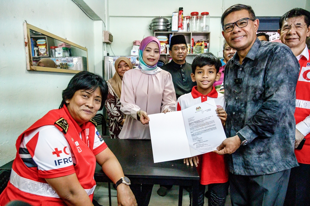 Home Minister Datuk Seri Saifuddin Nasution (right) hands over citizenship decision letters to Muhammad Danish Haiqal Abdul Rahman at Flat Sri Kelantan in Kuala Lumpur.  Also present was MRCS national chairman Tan Sri Tunku Puteri Intan Safinaz Sultan Abdul Halim Mu’adzam Shah (left) on July 18, 2024. — Picture by Firdaus Latif