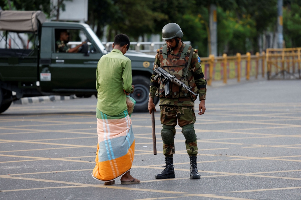 A member of the Bangladesh Army interrogates a man who came outside during a curfew imposed in response to student-led protests against government job quotas, in Dhaka, Bangladesh, July 20, 2024. — Reuters pic