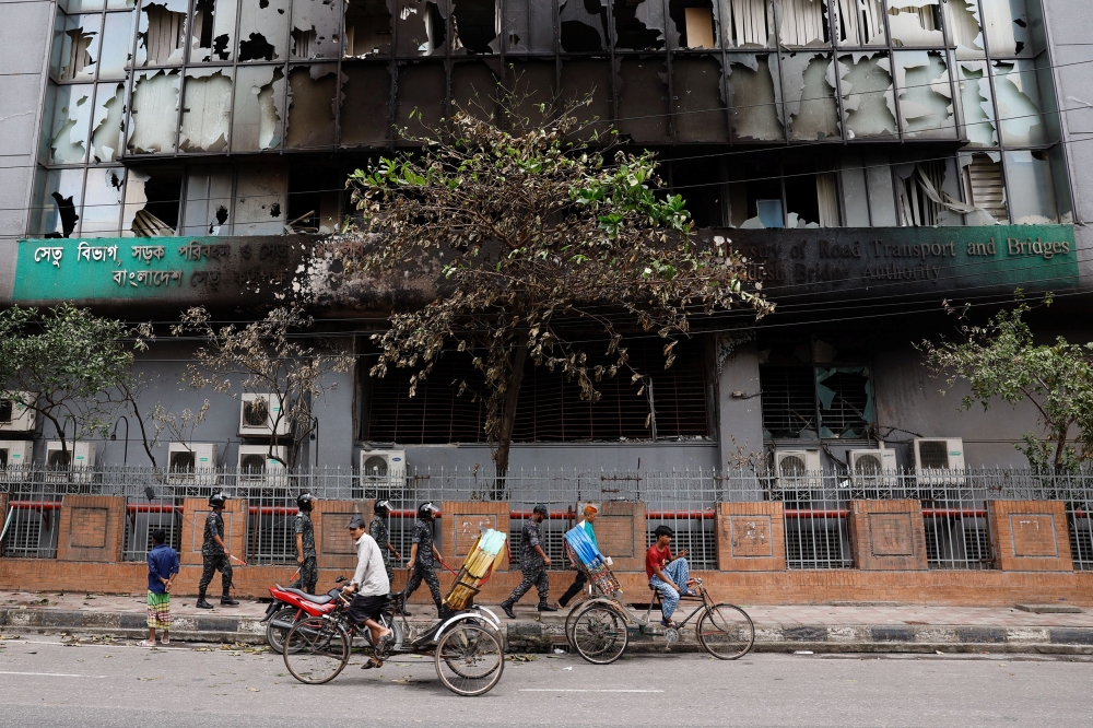Security personnel and rickshaw pullers move past a partially damaged government building, that was set afire by a mob during clashes after violence erupted following protests by students against government job quotas, in Dhaka, Bangladesh, July 22, 2024. — Reuters pic 