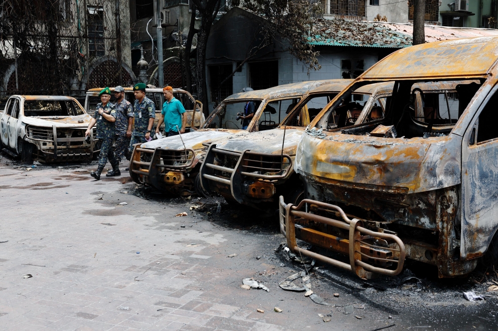 Security personnel walk past damaged vehicles that were set afire by a mob during clashes after violence erupted following protests by students against government job quotas, in Dhaka, Bangladesh on July 22, 2024. — Reuters pic 
