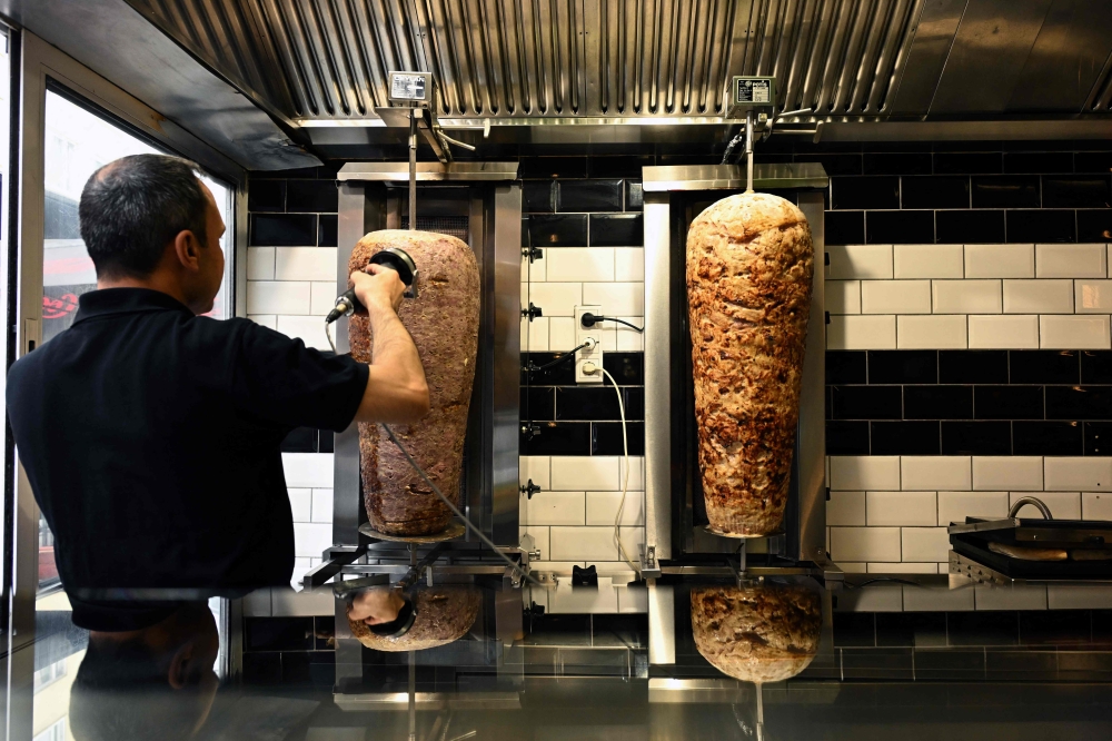 An employee scapes meat from a kebab skewer in a Doener restaurant in the city centre of Dortmund July 26, 2024. — AFP pic