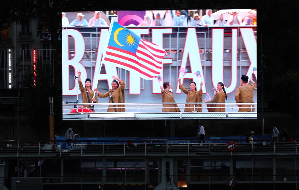 Betrand Rhodic Lises (far left) and Nur Shazrin Mohamad Latif hold up Malaysia’s flag during the opening ceremony of the Olympic Games in Paris, France on July 26, 2024. — Bernama pic