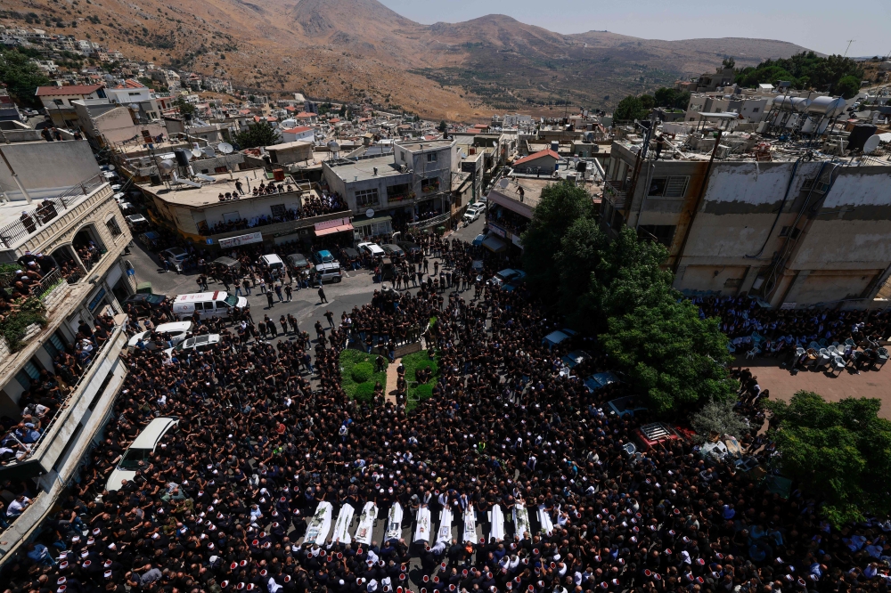 Druze elders and mourners surround the coffins of 10 of the 12 people killed in a rocket strike from Lebanon a day earlier, during a mass funeral in the Druze town of Majdal Shams in the Israel-annexed Golan Heights, on July 28, 2024. — AFP pic