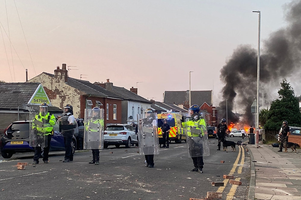 Smoke billows from a fire started by protesters as riot police stand guard after disturbances near the Southport Islamic Society Mosque in Southport, northwest England, on July 30, 2024. — AFP pic