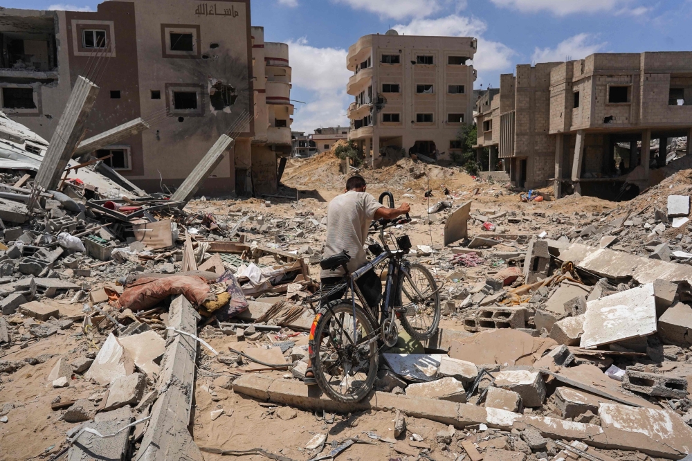 A man pushes his bicycle over rubble as displaced Palestinians return to Bani Suhayla and neighbouring towns east of Khan Yunis following reports of Israeli forces withdrawing from the area in the southern Gaza Strip on July 30, 2024. — AFP pic