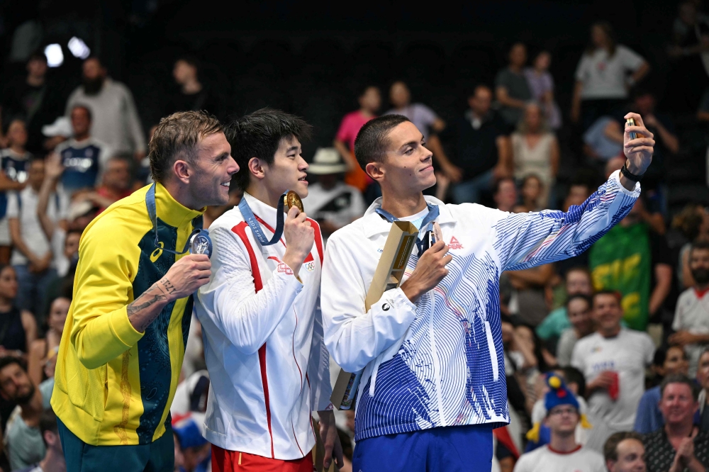 Silver medallist Australia's Kyle Chalmers (left), gold medallist and world record holder China's Pan Zhanle (centre) and Romania's David Popovici (right) takes a selfie on the podium of the men's 100m freestyle swimming event during the Paris 2024 Olympic Games at the Paris La Defense Arena in Nanterre, west of Paris, on July 31, 2024. — AFP pic