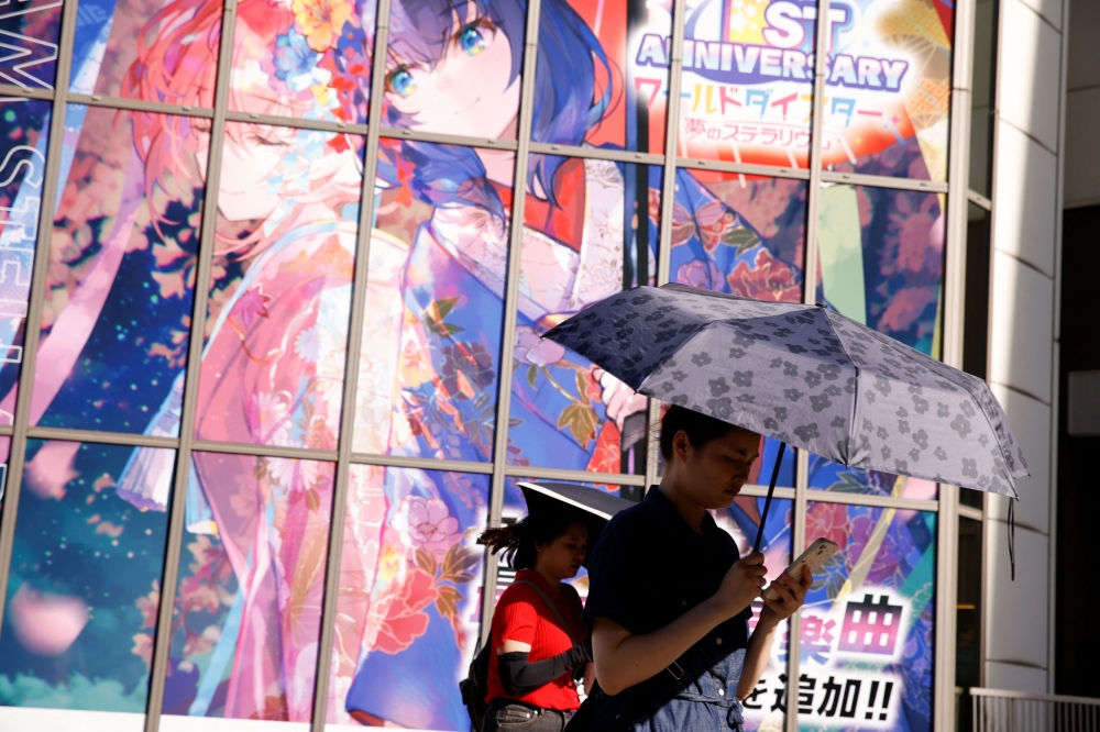 Women with umbrellas walk by a poster in Akihabara, as Japanese government issued heat stroke alerts in the country's prefectures in Tokyo. — Reuters pic