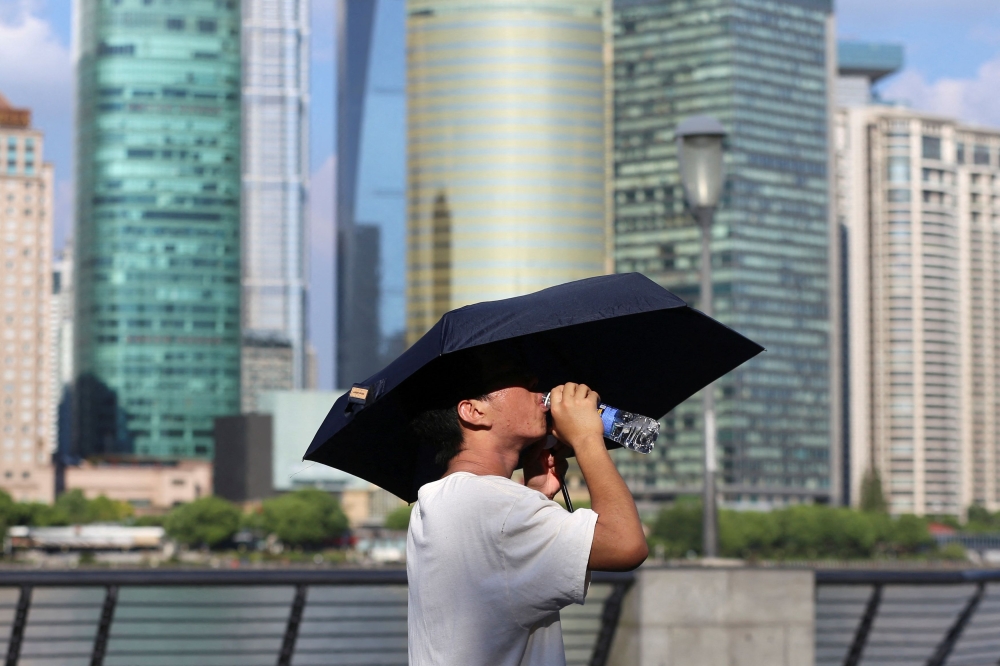 A man drinks from a water bottle under an umbrella as he walks on The Bund amid a red alert for heatwave, in Shanghai August 1, 2024. — Reuters pic