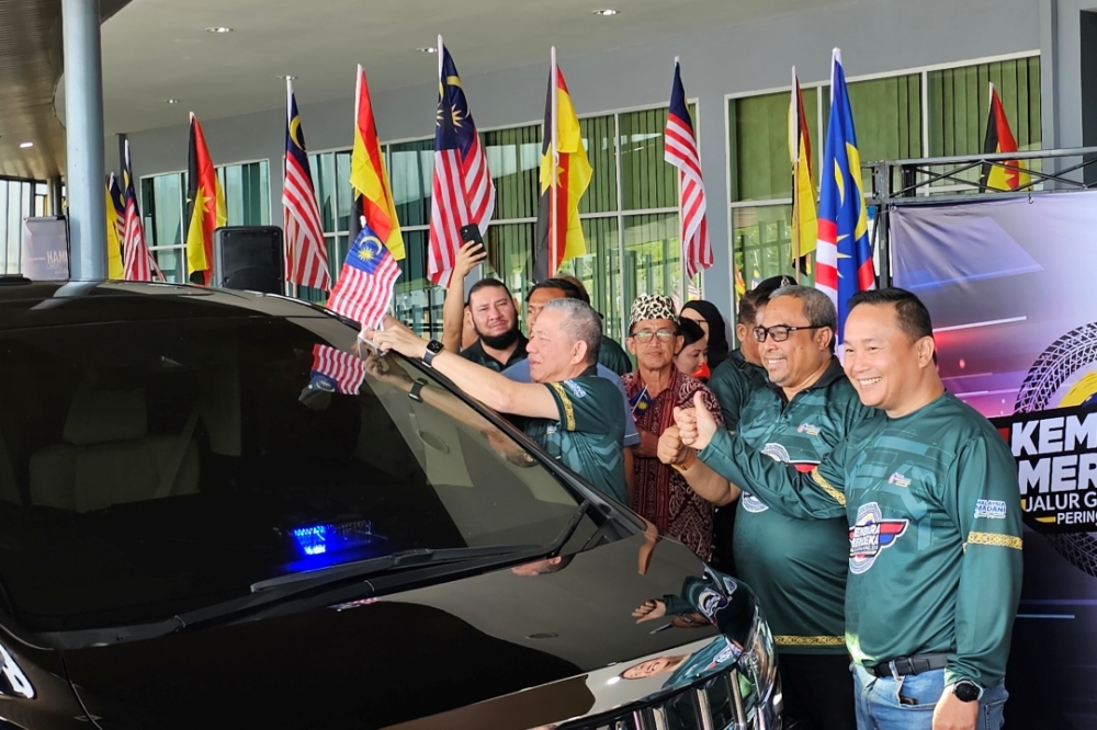 Fadillah attaches a Jalur Gemilang on a vehicle participating in a convoy, one of the National Month 2024 activities being run in Sarawak. — The Borneo Post pic