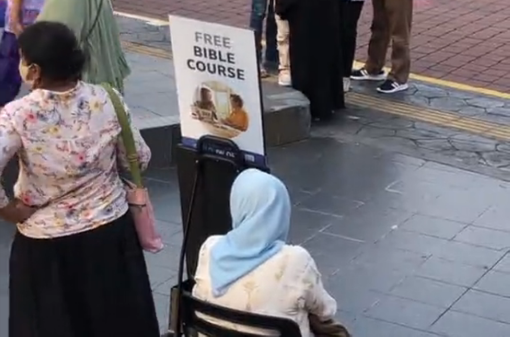 A screen capture of a video circulating online shows two people manning a standee with materials for a “free bible course” in Bandar Hilir, Melaka. 