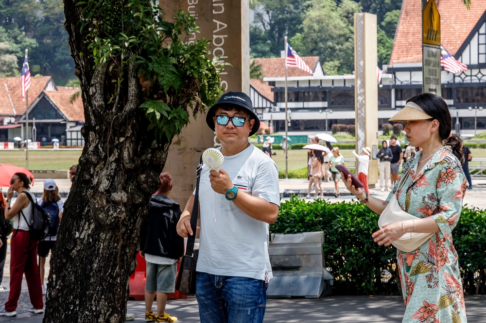 A man using a portable mini fan to cool himself in the tree shade near Merdeka Square during a heatwave in Kuala Lumpur on July 30, 2024. — Picture by Firdaus Latif