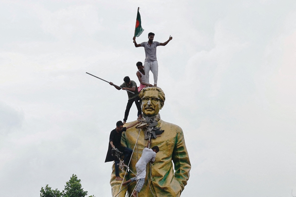 People climb the statue of Sheikh Mujibur Rahman at the Bijoy Sarani area, as they celebrate the resignation of the Prime Minister Sheikh Hasina in Dhaka, Bangladesh, August 5, 2024. — Reuters pic