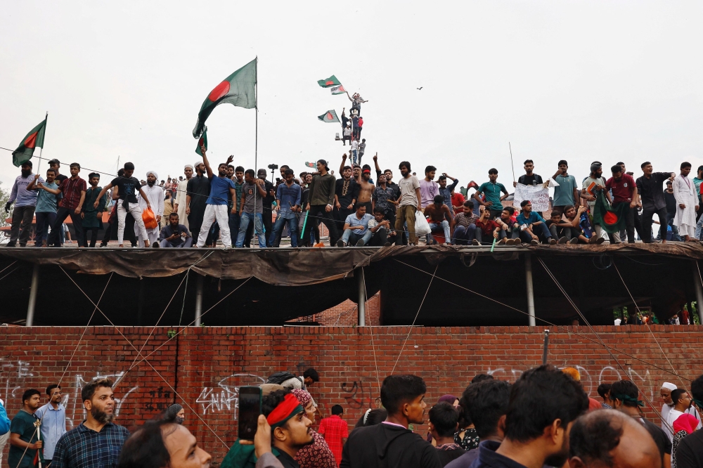 People waves Bangladeshi flags on top of the Ganabhaban, the Prime Minister's residence, as they celebrate the resignation of PM Sheikh Hasina in Dhaka, Bangladesh, August 5, 2024. — Reuters pic