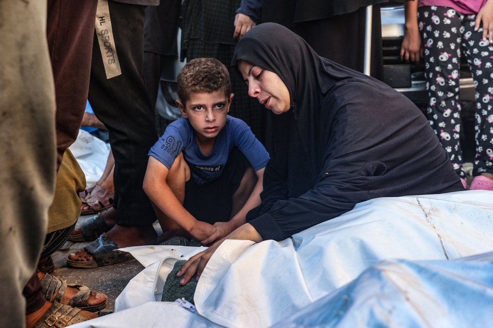 A child looks on as a woman mourns over the corpse of a member of her family killed in an overnight Israeli strike, in the yard of the Al-Aqsa Martyrs hospital in Deir el-Balah in the central Gaza Strip on August 10, 2024. — AFP pic