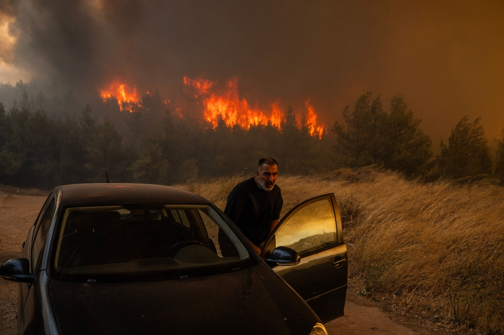  A local gets into his car in front of the flames to evacuate during a wildfire in Dione on August 12, 2024. On August 12, 2024. — AFP pic