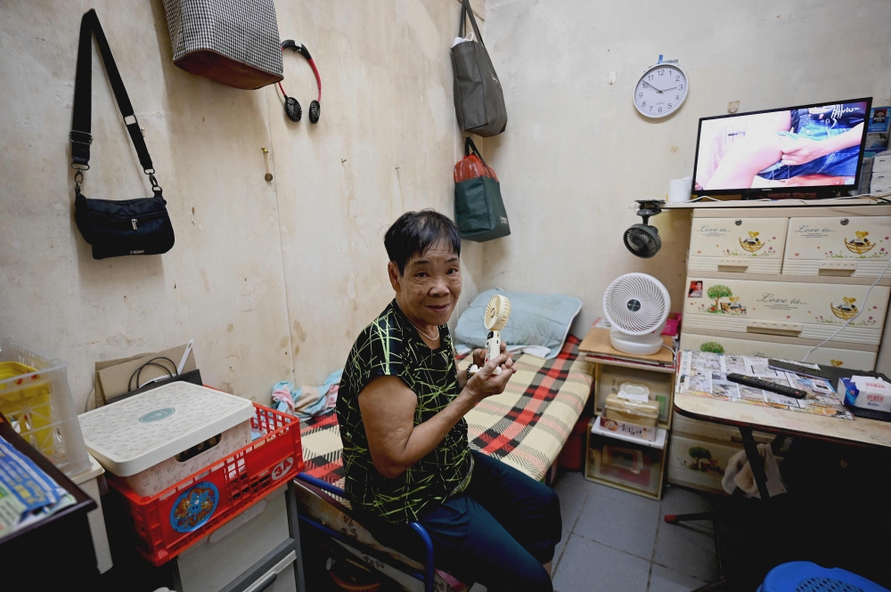 This photo taken on August 10, 2024 shows retired janitor Chun Loi, 84, sitting on her bed while facing electric fans inside her 50-square-foot windowless one-room flat in Hong Kong. — AFP pic