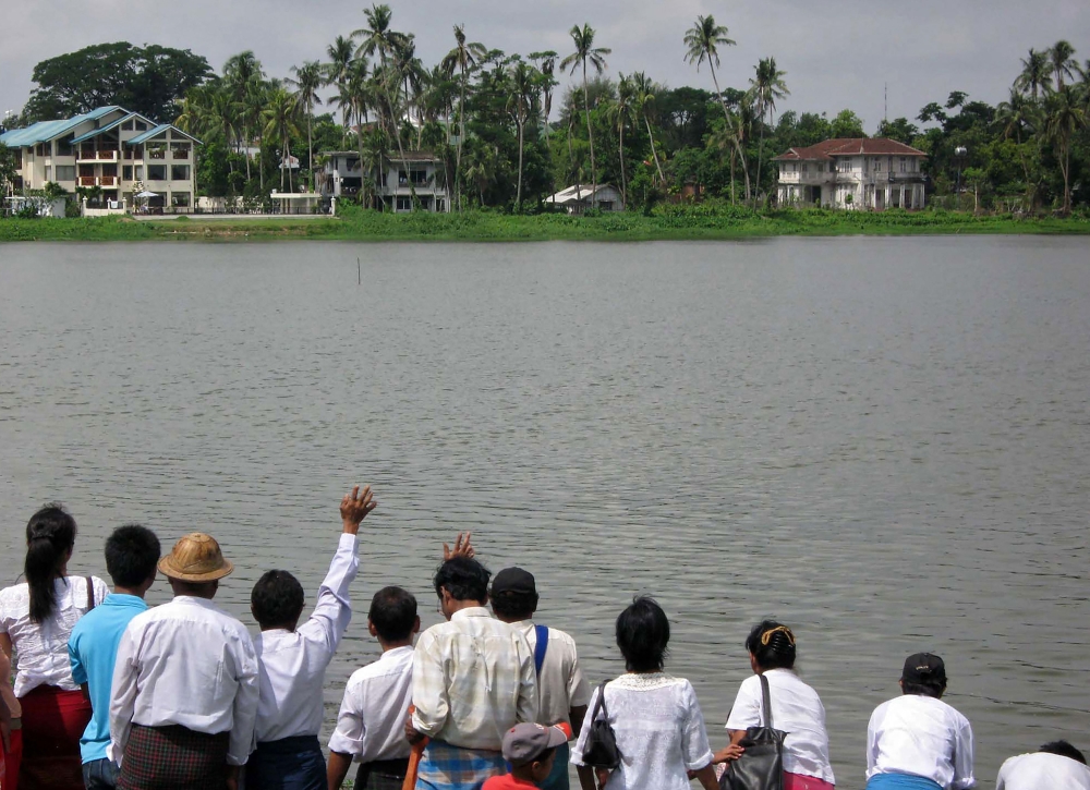 Supporters of Myanmar's detained democracy leader Aung San Suu Kyi wave towards her house (R, with red roof house) at Inya Lake in Yangon on April 17, 2009. — AFP pic